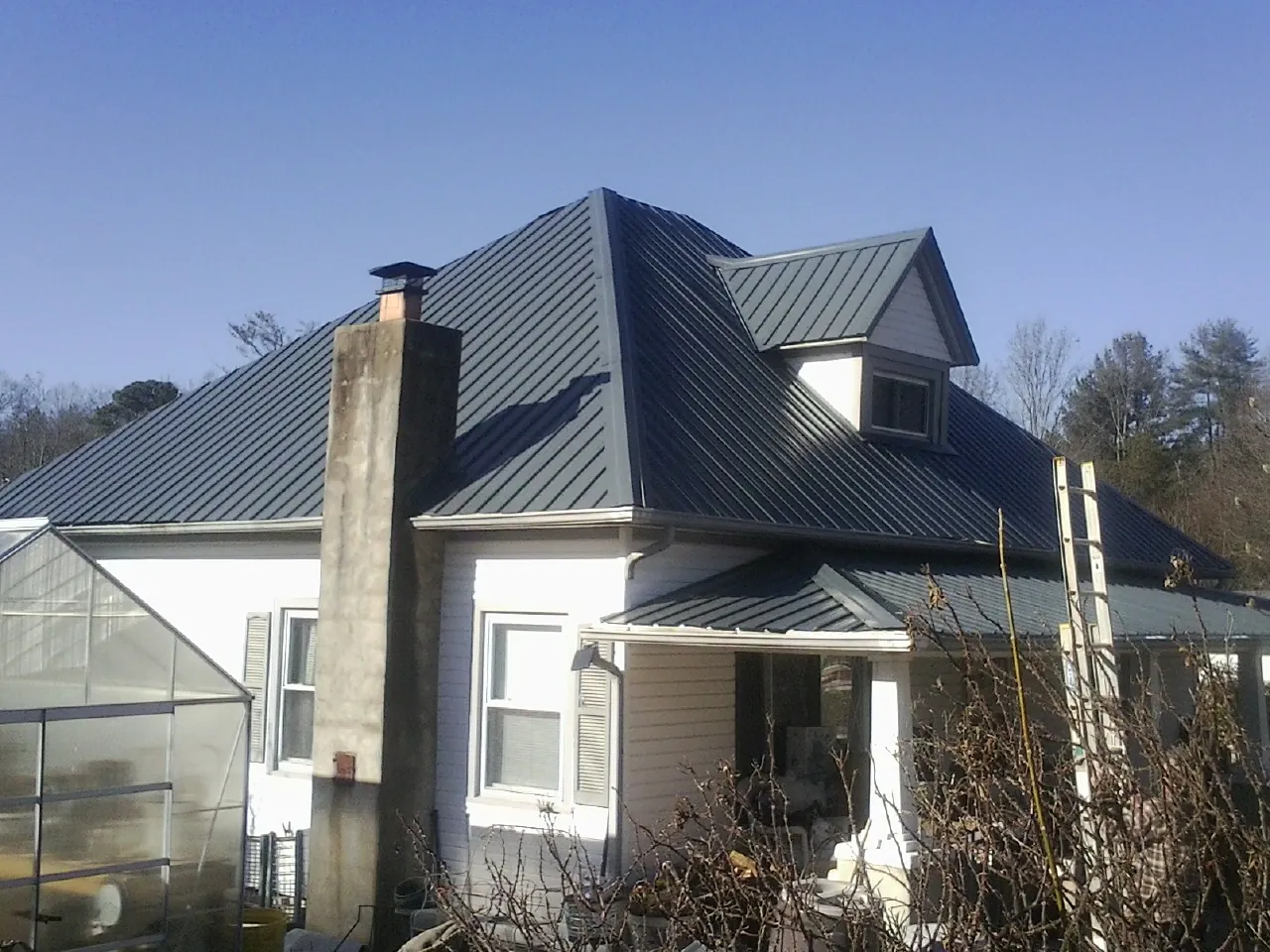 Dark blue standing seam metal roof on a white farmhouse with dormer — Slate & Tile Roof Repair by Roofing Brothers in Splendora
