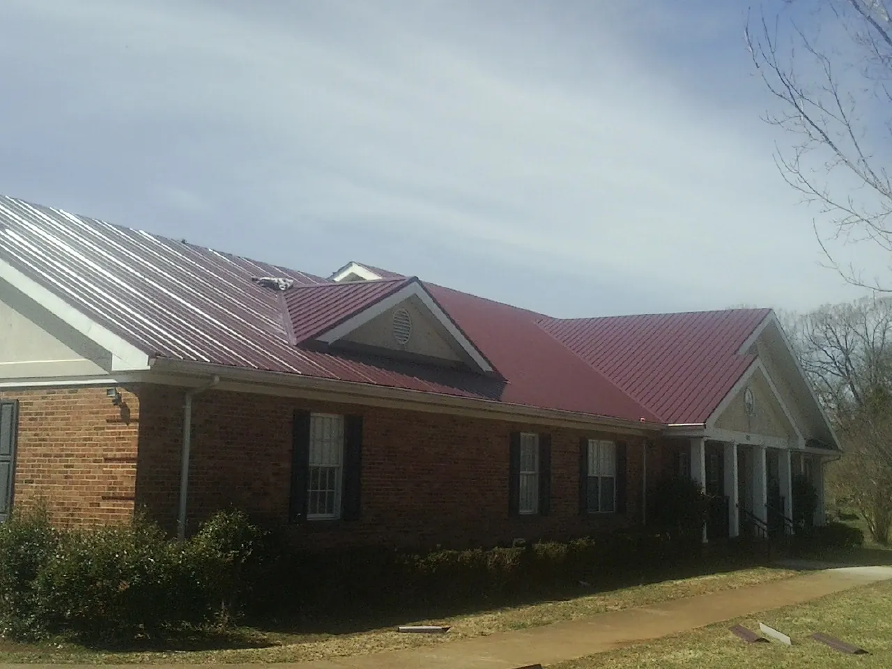 Red metal roof with gabled entries on a long brick building, from a Hail Damage Roof Repair job in Splendora