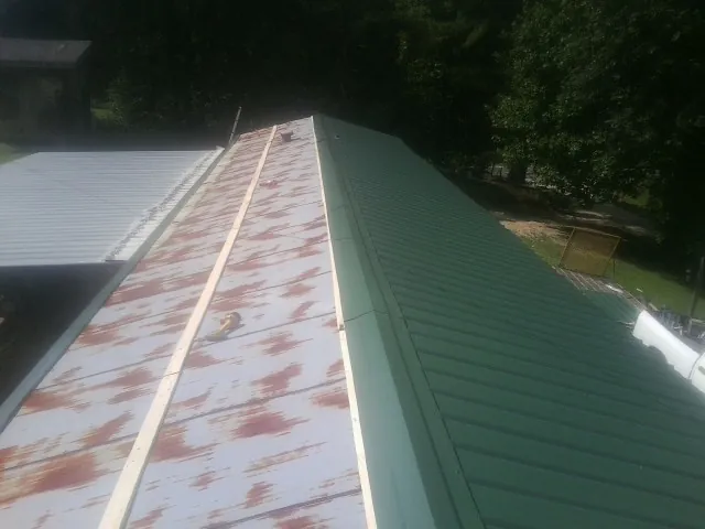 Old rusted panels beside newly installed green metal roofing — Wind Damage Roof Repair by Roofing Brothers in Splendora
