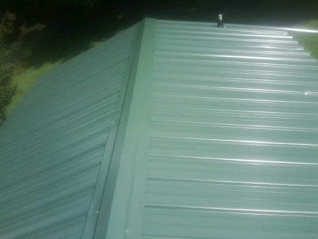 New green metal panels meeting at the ridge of a roof — Flat Roof Repair work by our crew in Splendora