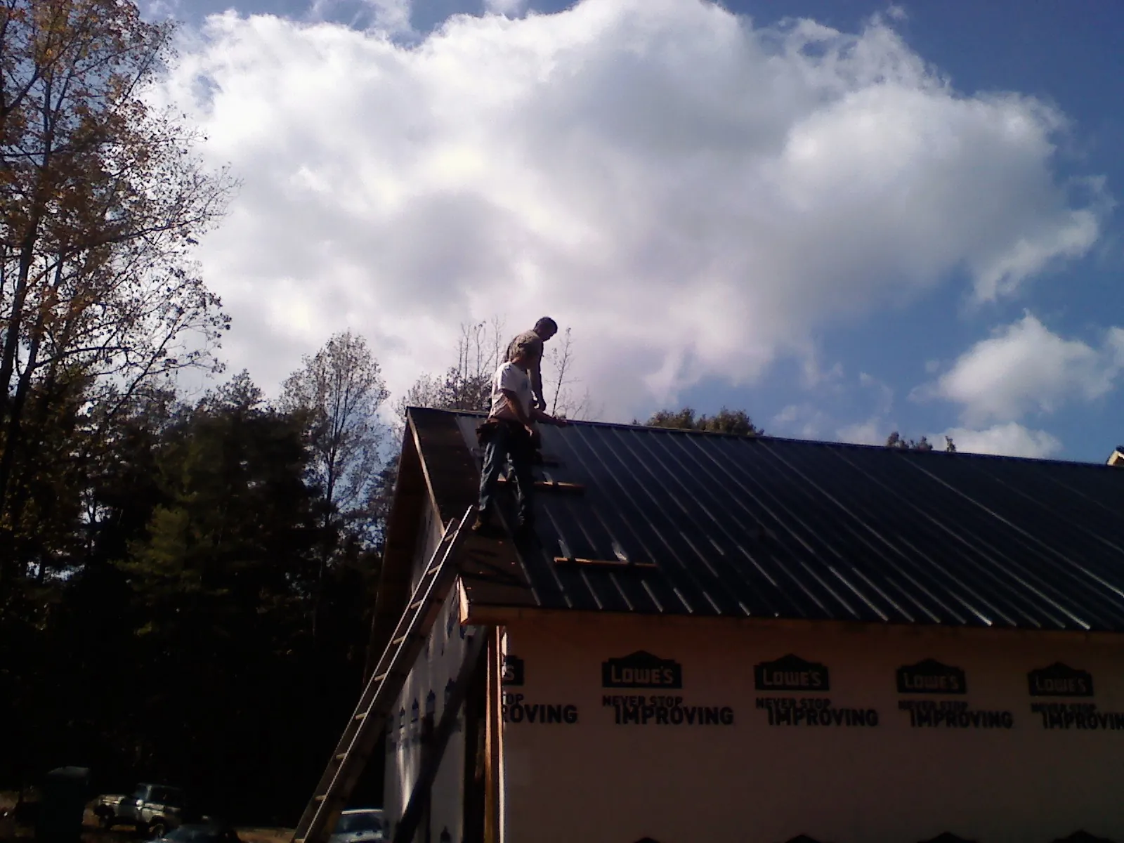 Roofer fastening dark metal panels high against a cloudy sky, from a Roof Inspection job in Splendora