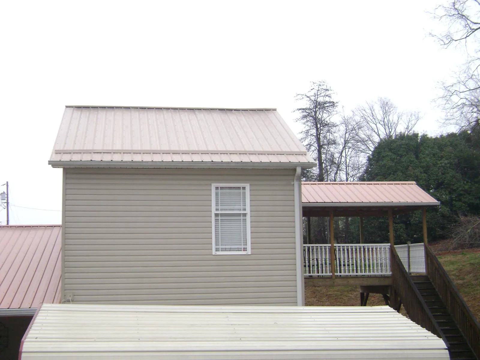 Tan metal roofs on a two story addition and attached porch, from a Roof Replacement job in Splendora
